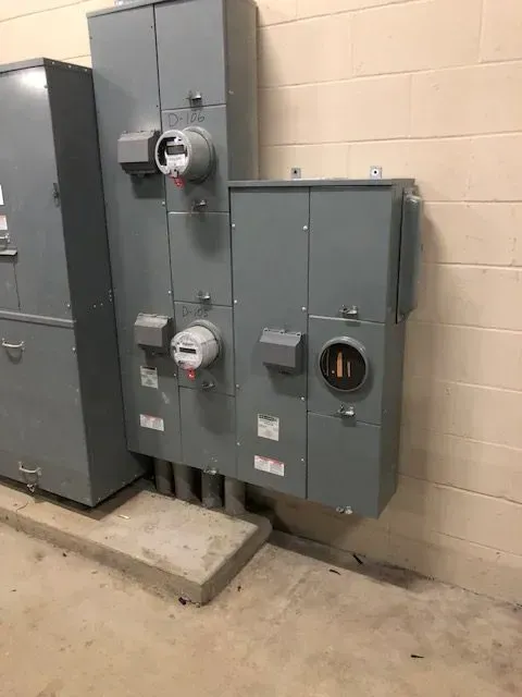 Electrical utility boxes mounted on a wall. Gray metal boxes house meters and electrical components in a concrete setting.