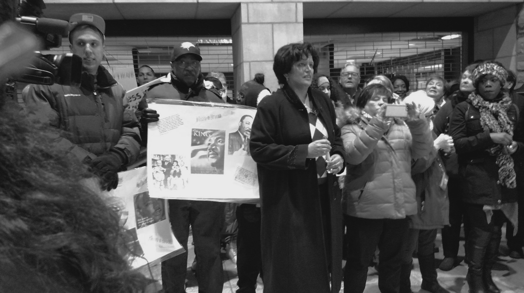 People holding signs, gathered outdoors under an overhang.