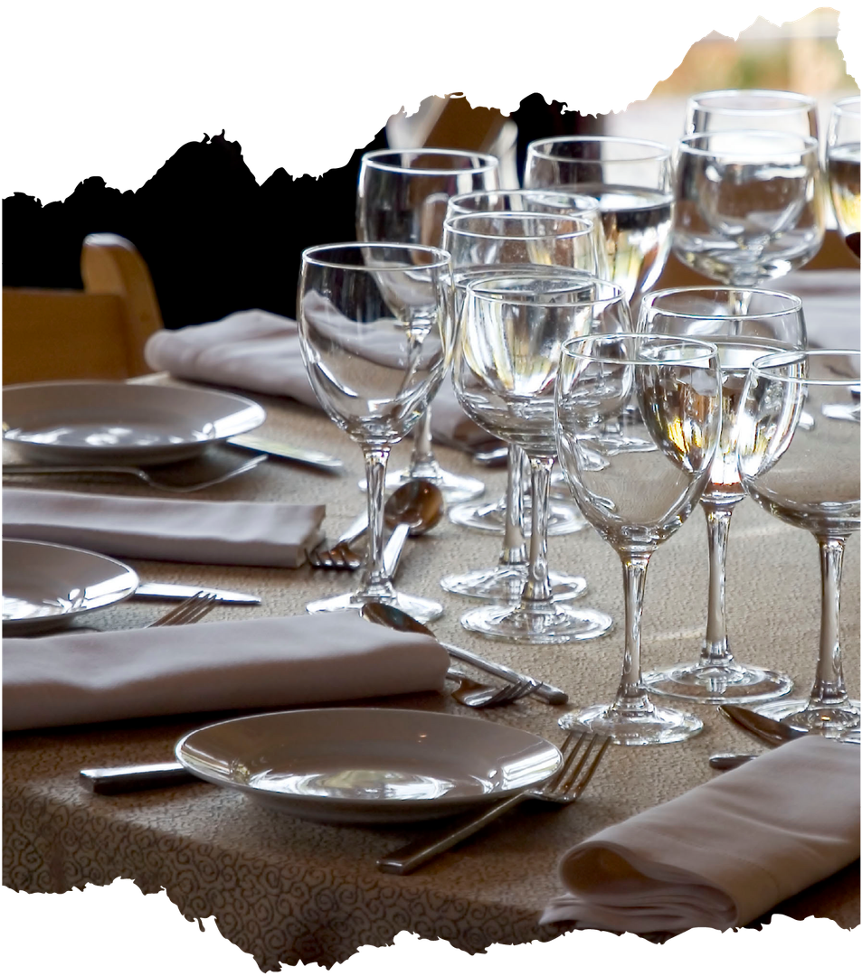 Table set for a meal: plates, silverware, napkins, and multiple water and wine glasses.