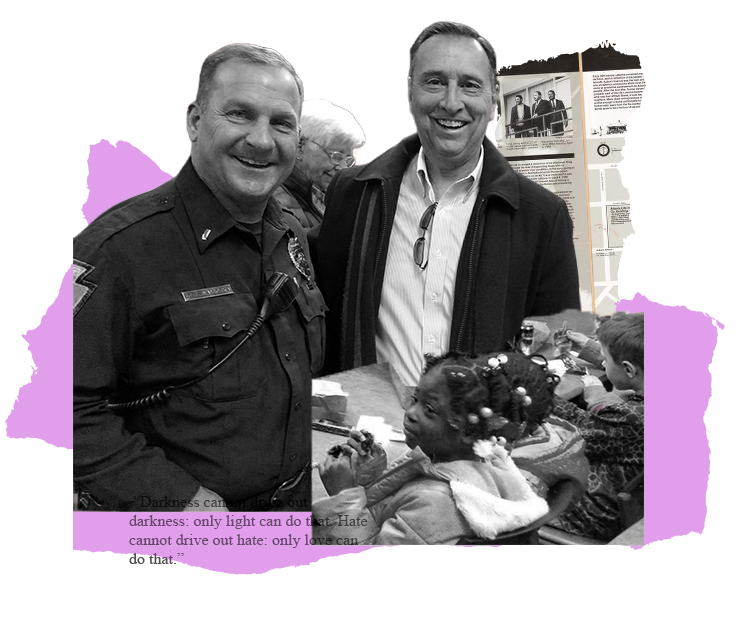 Two men smile at the camera. One in a police uniform, the other in a jacket. They are near a display.