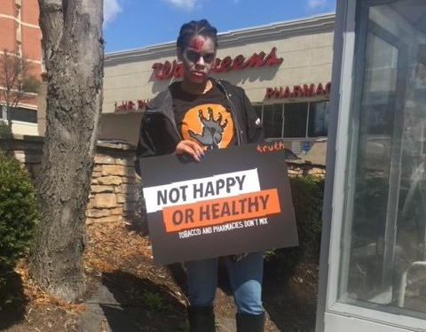 brittaney jenkins participating in a public health campaign holding a Not Happy or Healthy sign in front of a Walgreens store
