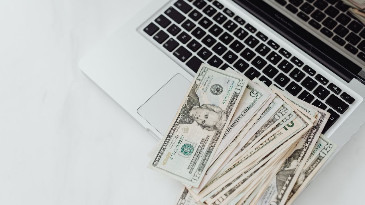 Cash spread over the keyboard of a black and white laptop
