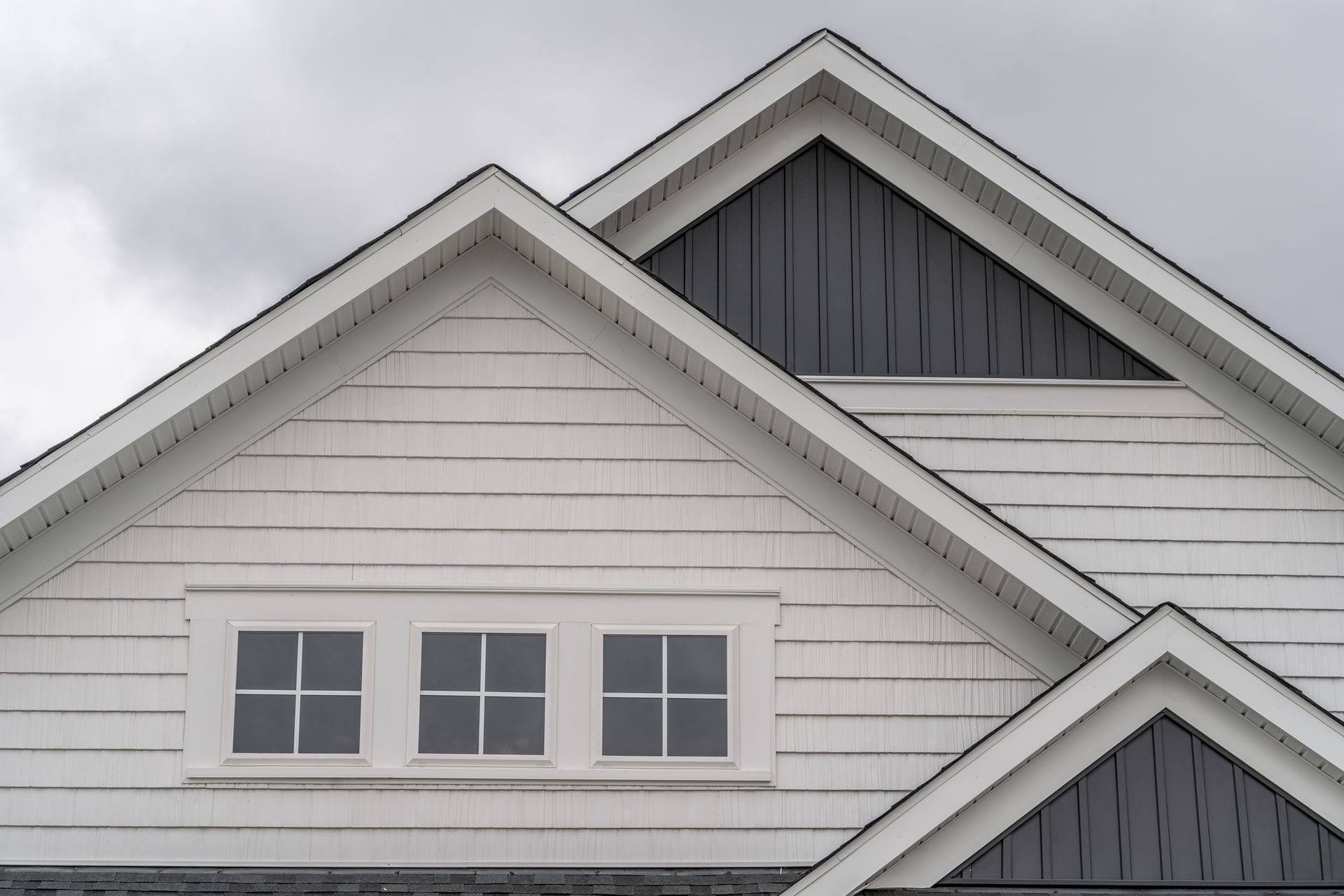 White house exterior with three windows, gray gabled roof, and dark gray siding.