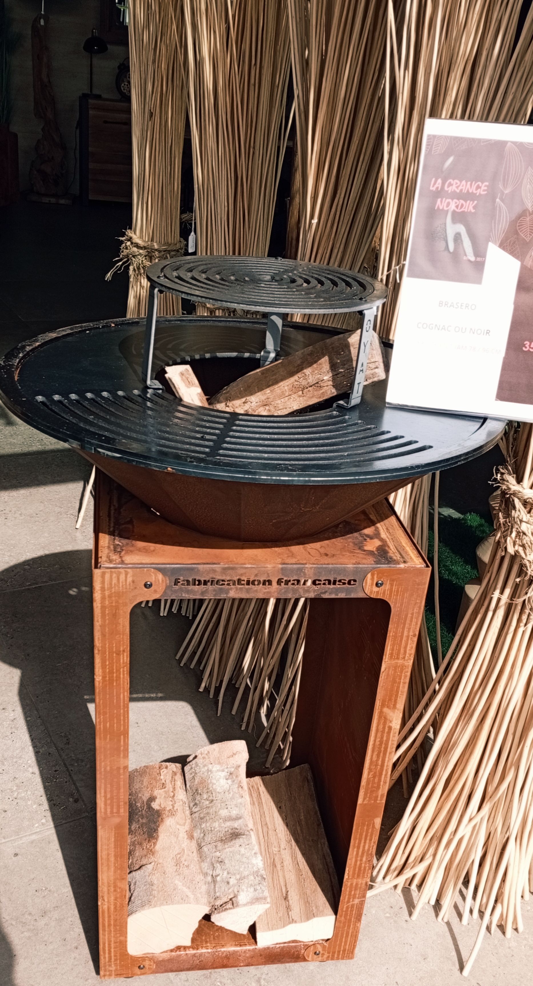 Foyer extérieur en métal rouillé avec grille, rangement pour le bois et combustible, par une journée ensoleillée.