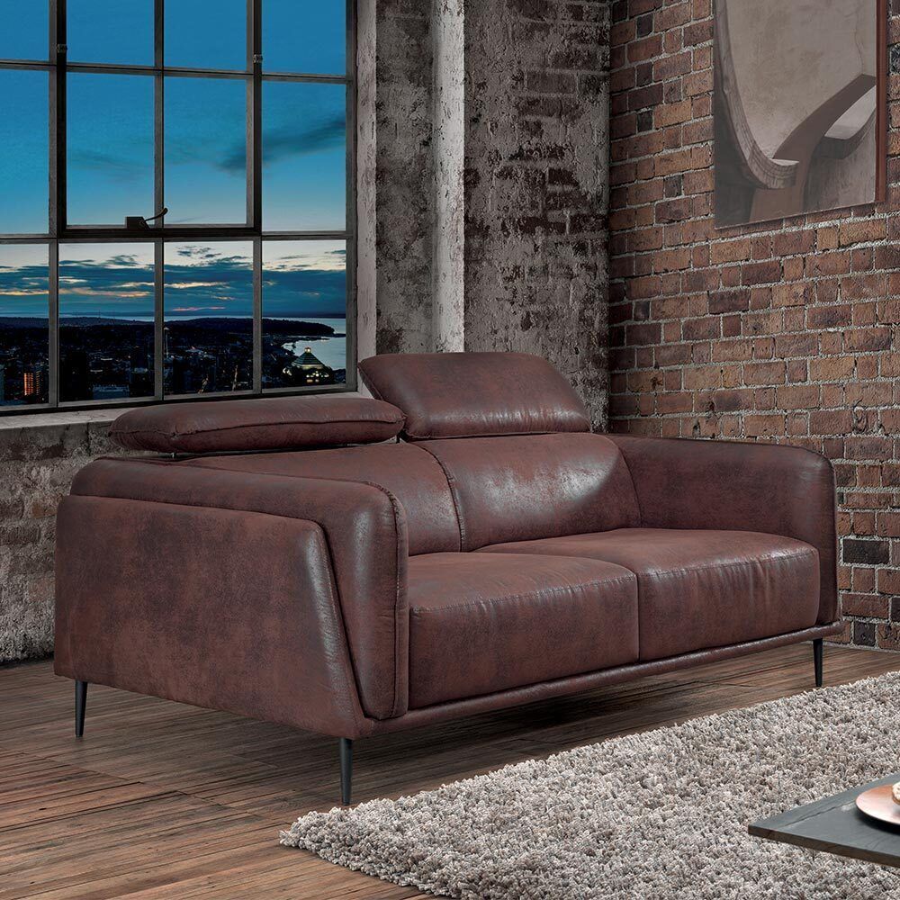 Canapé en cuir marron dans une pièce de style industriel avec un mur de briques et une fenêtre donnant sur un paysage urbain.