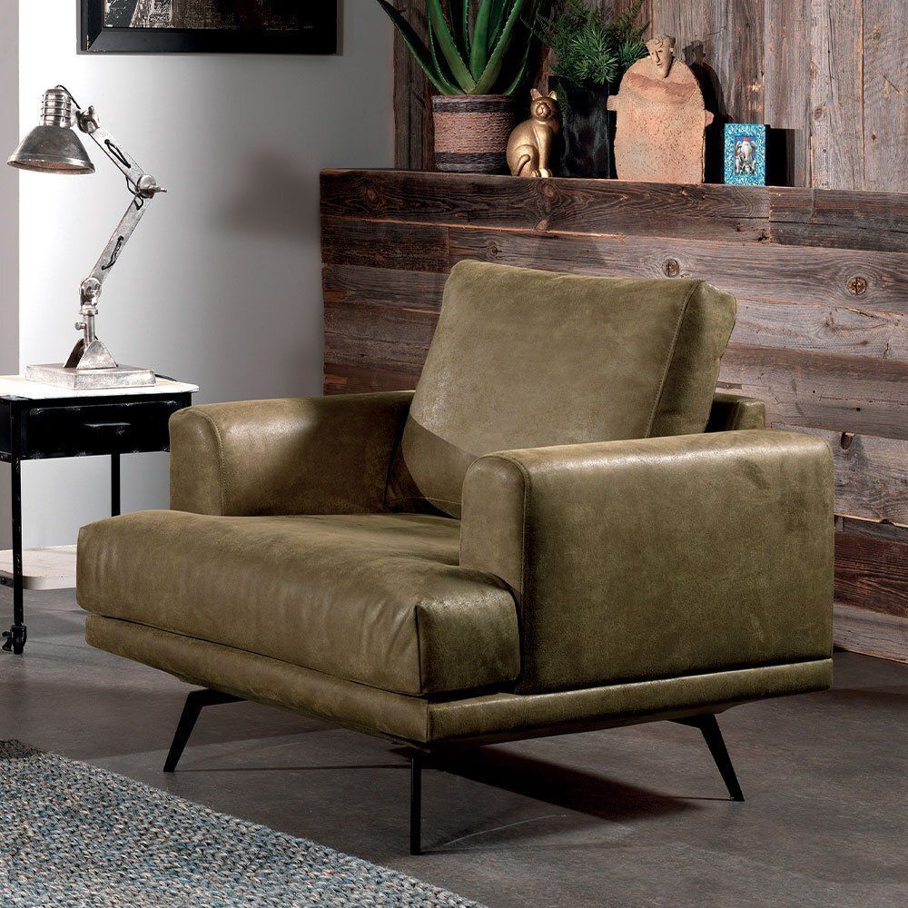 Fauteuil en cuir vert avec pieds en métal noir, placé dans une pièce avec une table d'appoint, une lampe et un mur en bois.