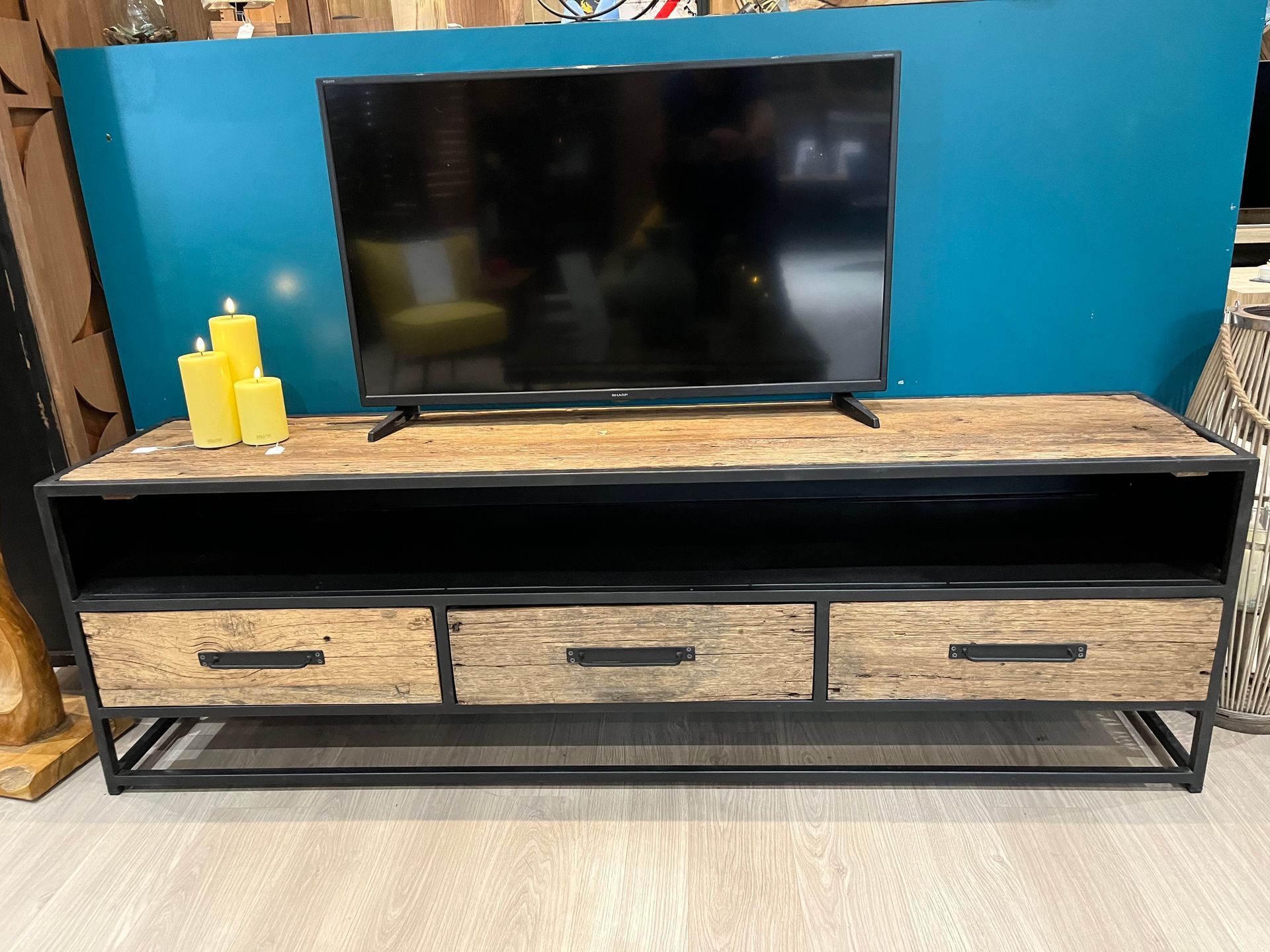 Téléviseur sur un meuble TV en bois avec tiroirs et étagère ouverte, adossé à un mur turquoise.