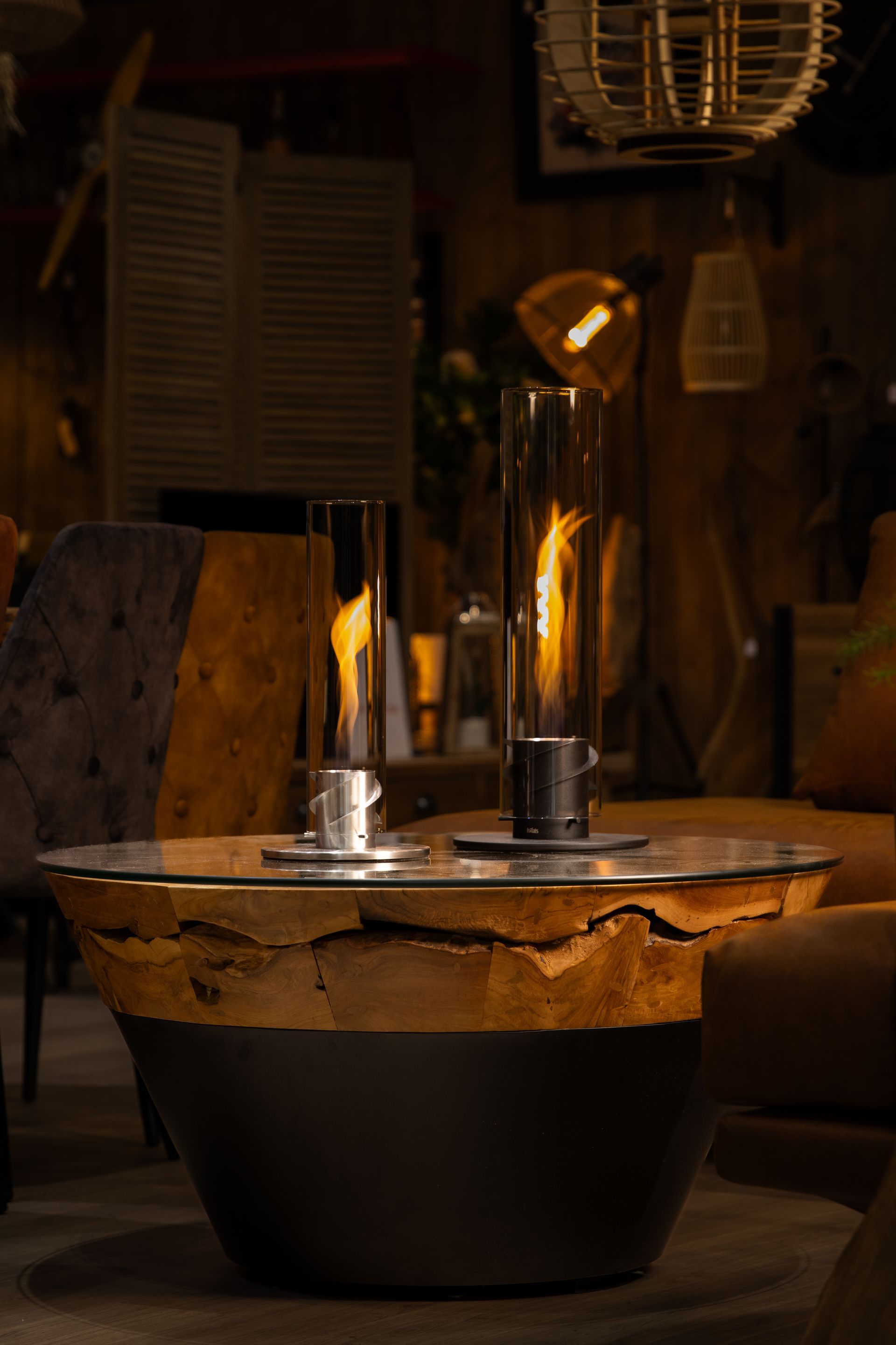 Deux cheminées de table allumées sur une table basse rustique en bois ; intérieur tamisé et chaleureux.