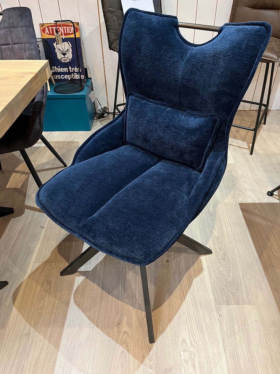 Fauteuil bleu capitonné avec dossier incurvé et coussin, sur un parquet.