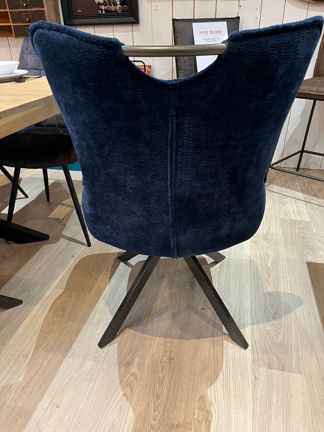 Fauteuil bleu capitonné avec dossier incurvé et coussin, sur un parquet.