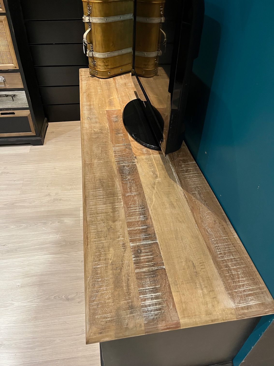 Meuble TV noir avec un téléviseur dessus, mur bleu turquoise en arrière-plan. Décoration : une lanterne et un bocal en métal.