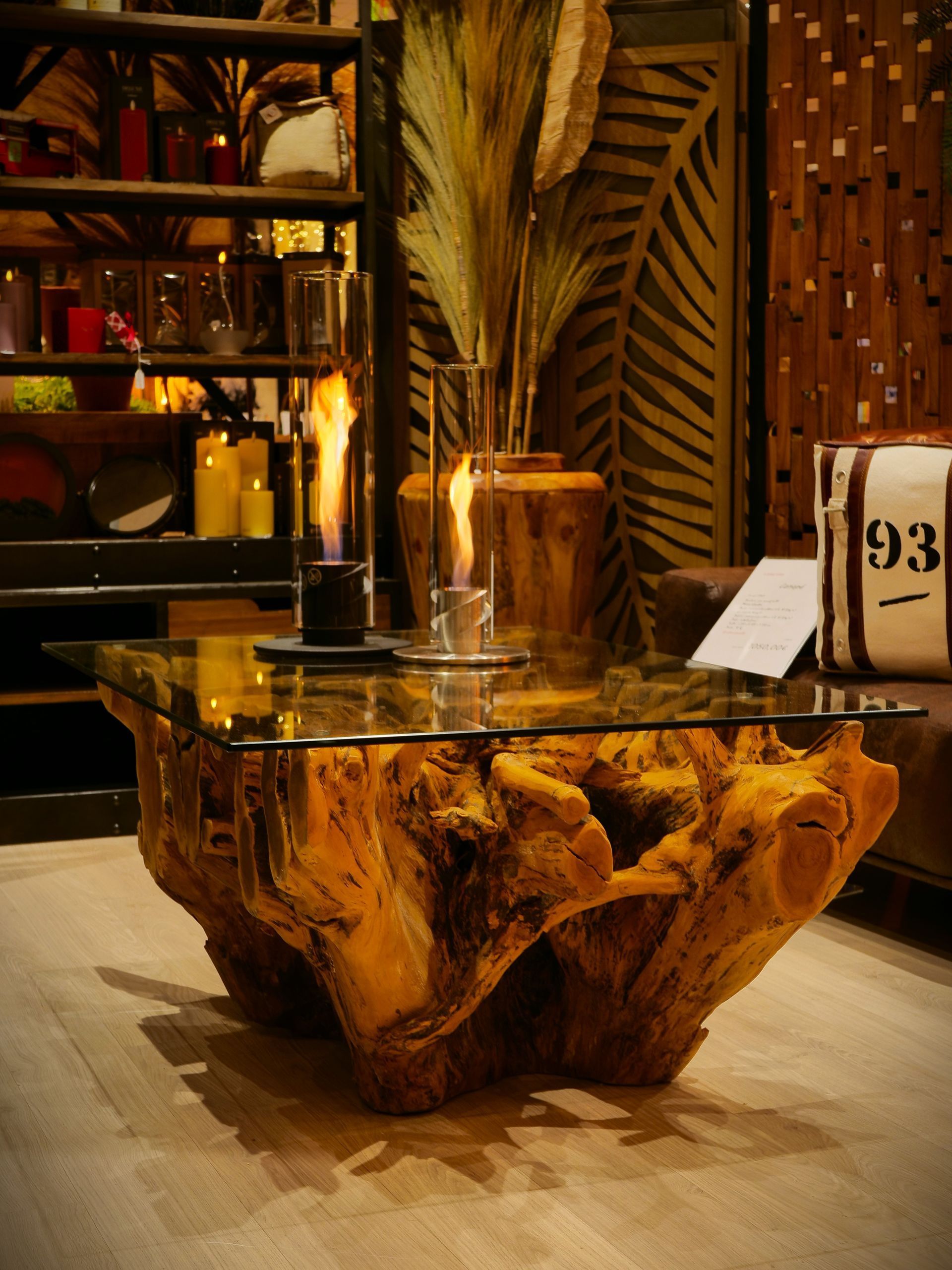 Table basse avec plateau en verre et piètement en bois texturé, ornée de deux lanternes à flamme.