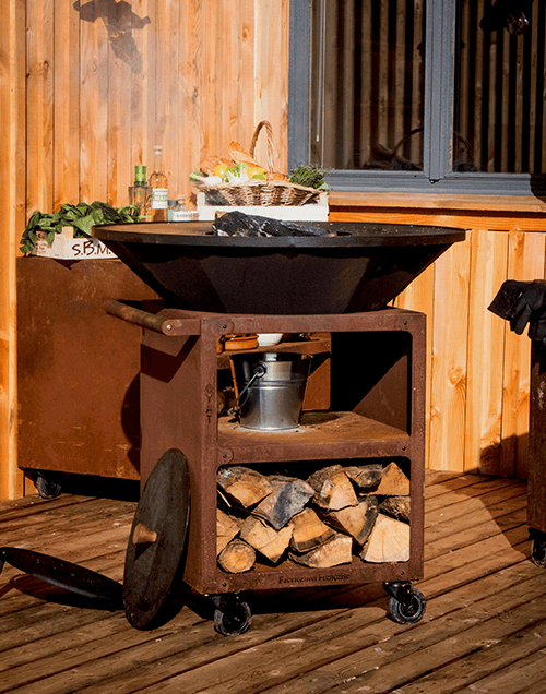 Poste de cuisson extérieur avec un bol de cuisson noir, une étagère de rangement en bois et un fond en bois.