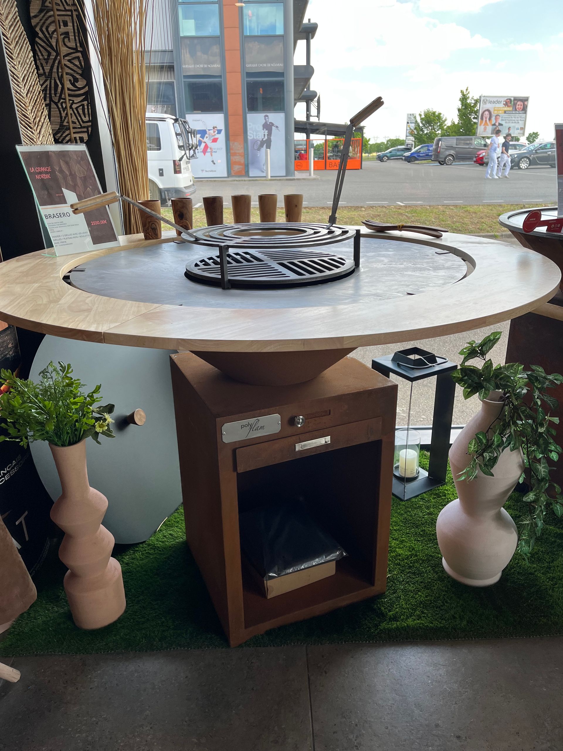 Table de barbecue ronde d'extérieur avec foyer intégré et armoire de rangement, sur gazon artificiel.