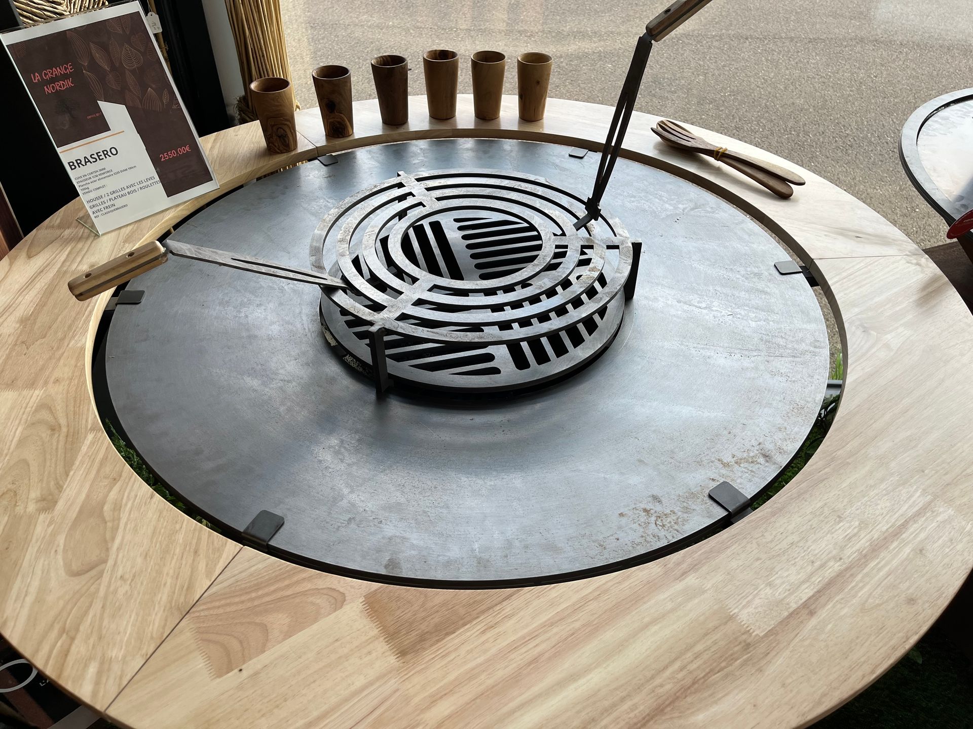 Table de barbecue ronde d'extérieur avec foyer intégré et armoire de rangement, sur gazon artificiel.