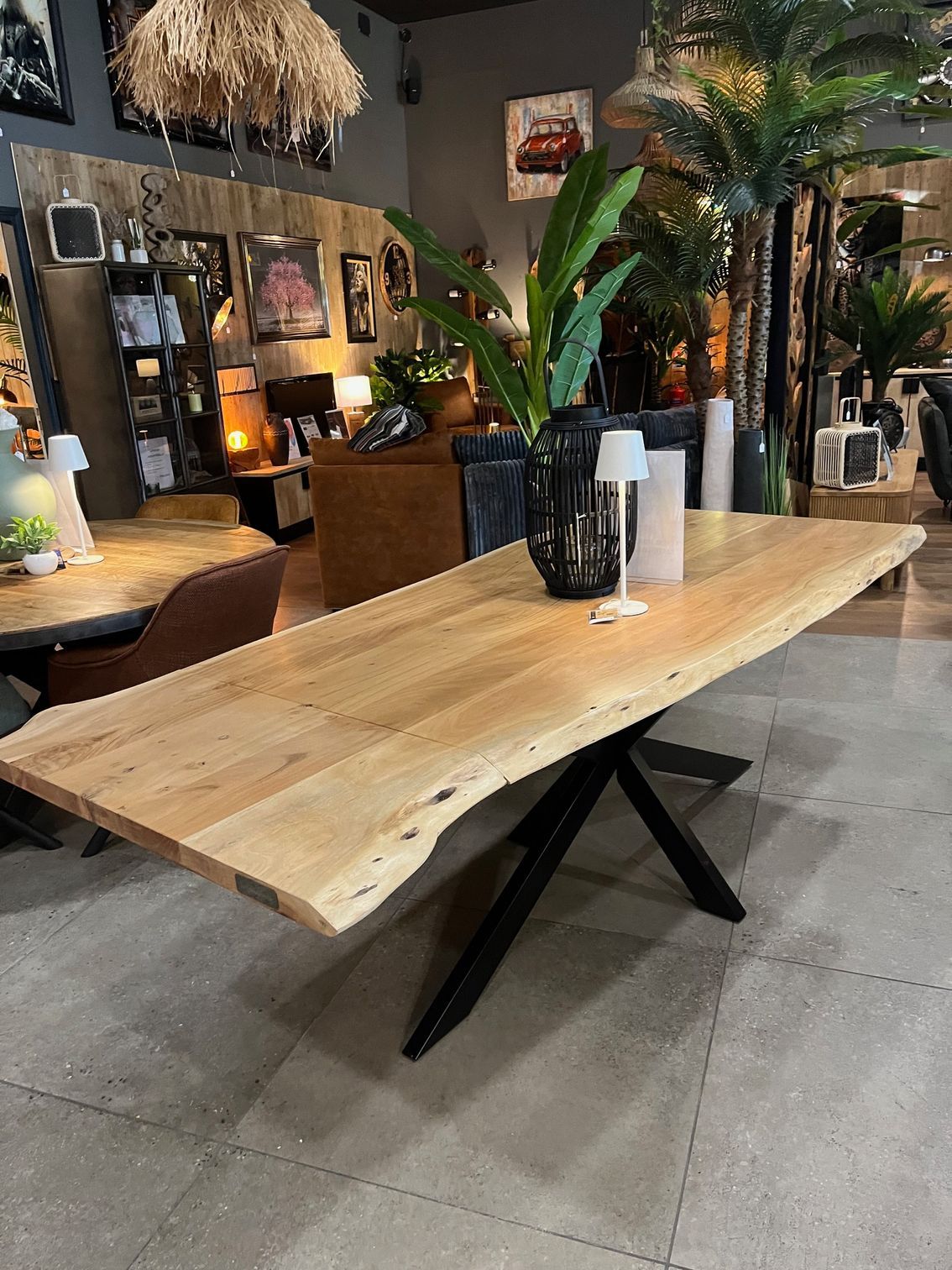 Table de salle à manger en bois clair avec pieds en métal noir, présentée dans un showroom.