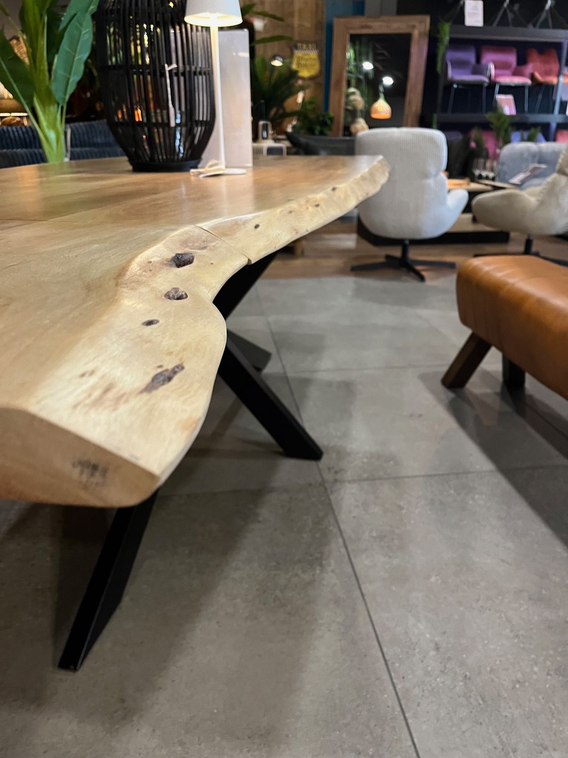 Table de salle à manger en bois clair avec pieds en métal noir, présentée dans un showroom.