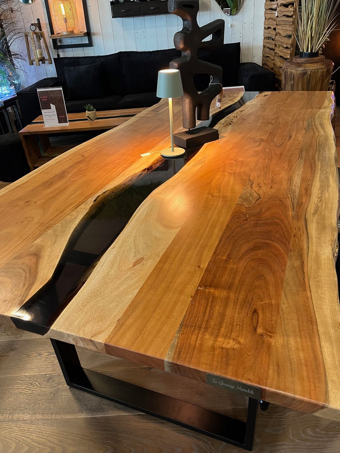 Table en bois avec rivière en époxy foncé et piètement en métal noir. Lampe et sculpture sur le dessus.