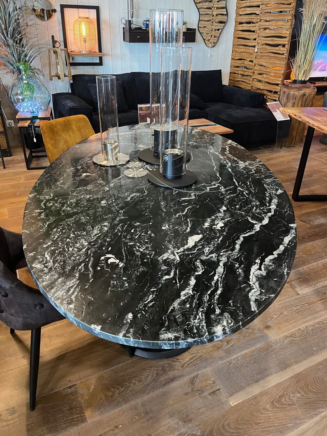 Table ronde en marbre noir avec cylindres de verre décoratifs et mobilier sombre dans une salle d'exposition.