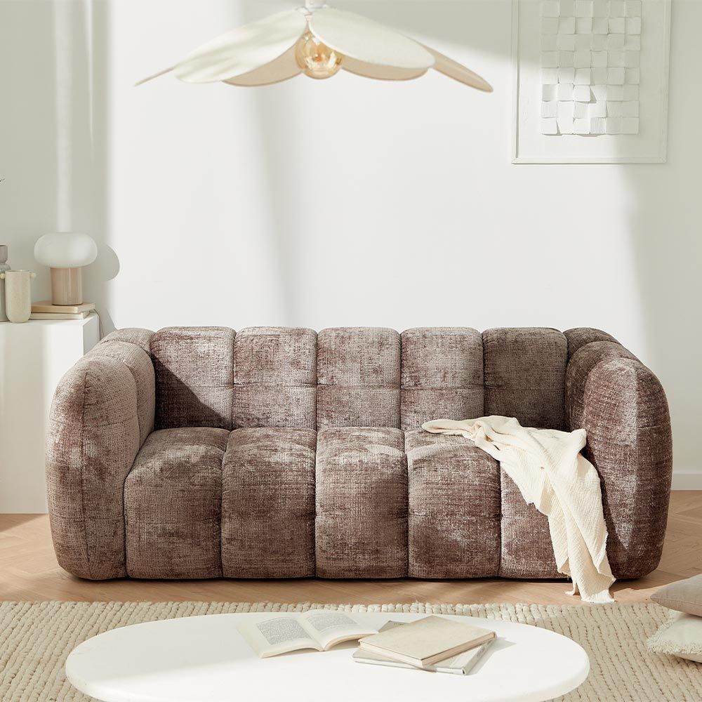 Canapé capitonné marron dans un salon moderne avec une table basse ronde et un plafonnier décoratif.