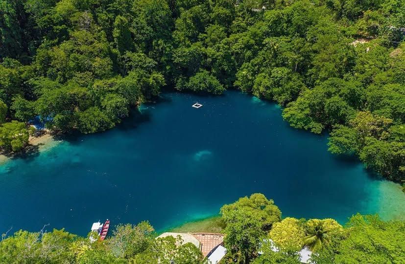 Blue lagoon surrounded by dense green forest, with a small boat near the center