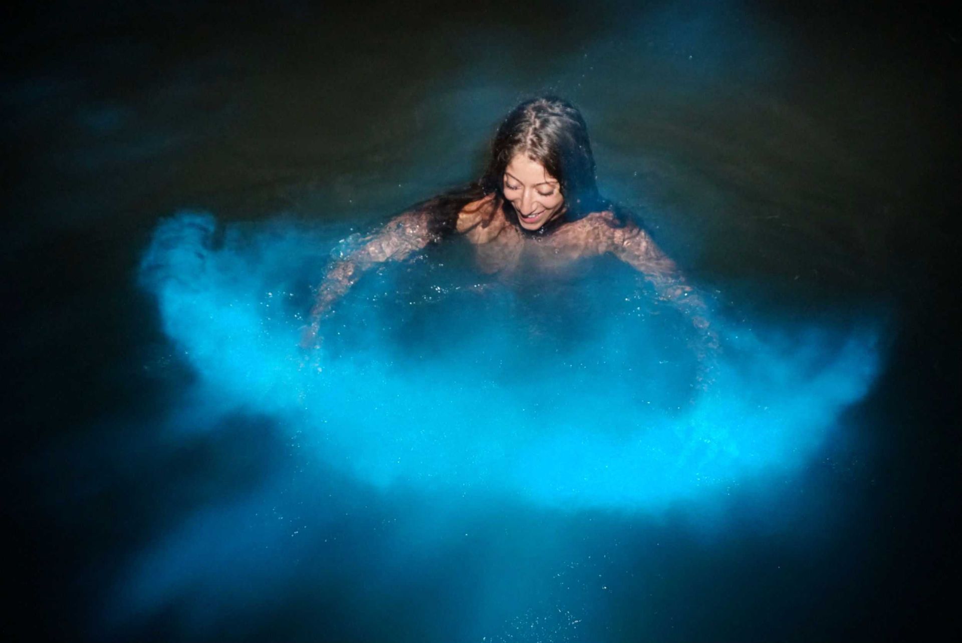 Person in dark water splashing bright blue powder around them
