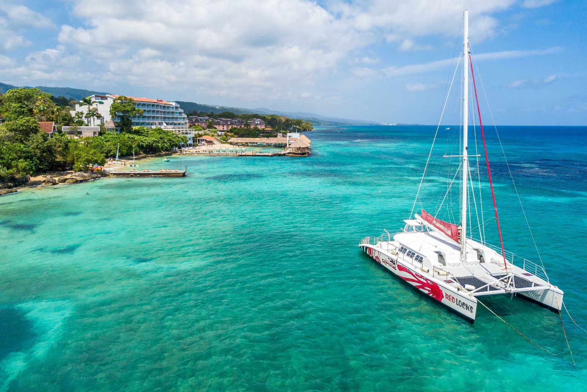Catamaran on turquoise tropical water near a coastal resort shoreline