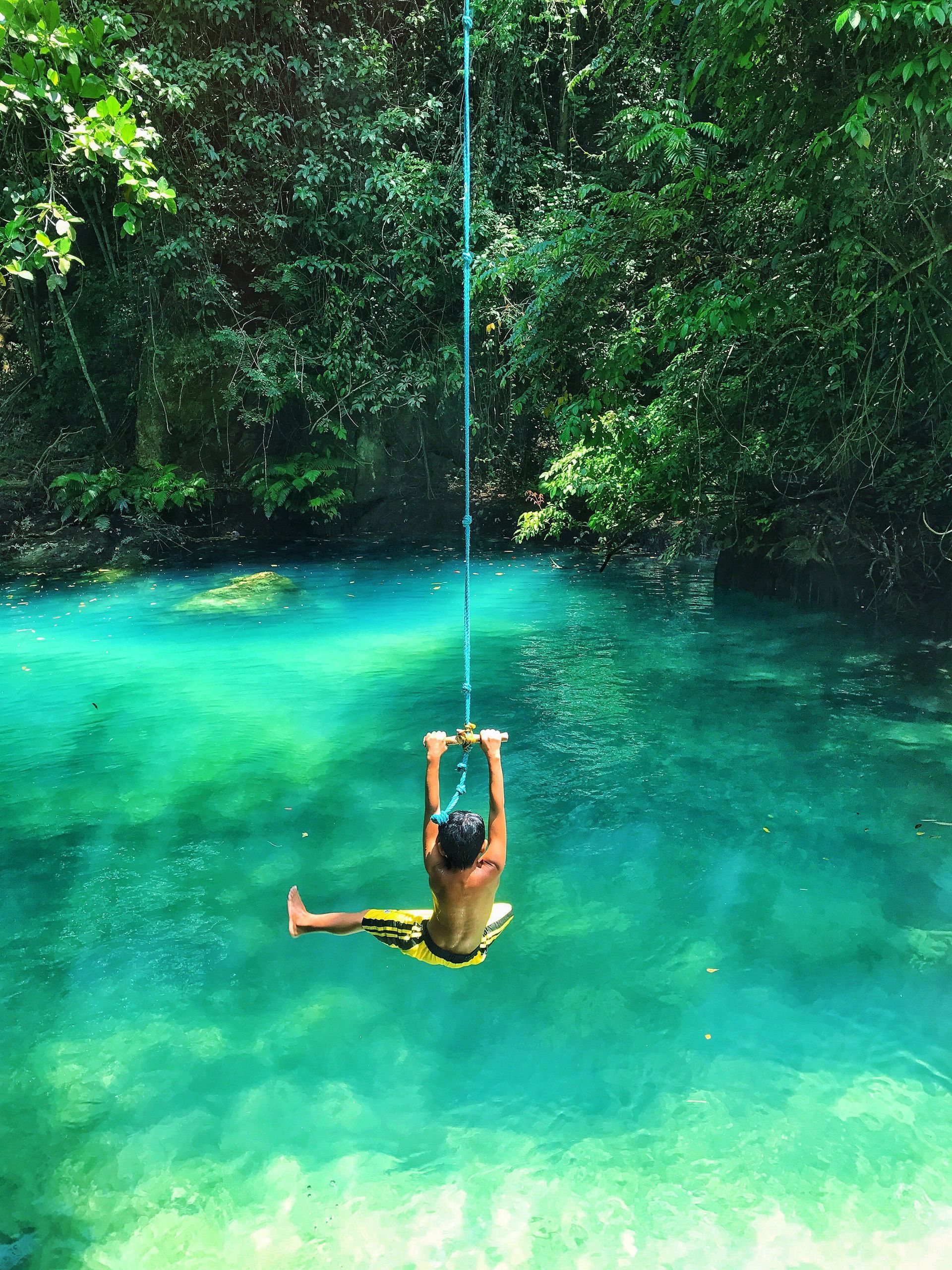 Person swinging on a rope over a turquoise jungle pool