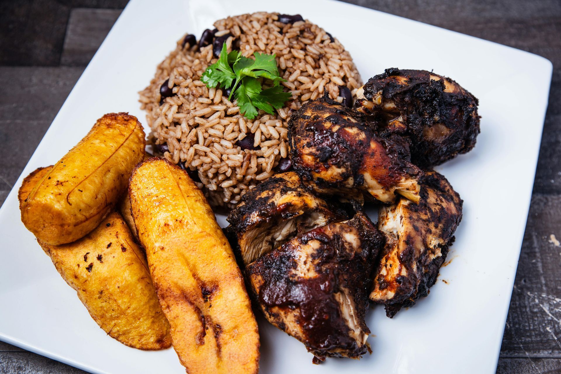 Plate of rice, grilled chicken, and fried plantains with parsley garnish on a white plate