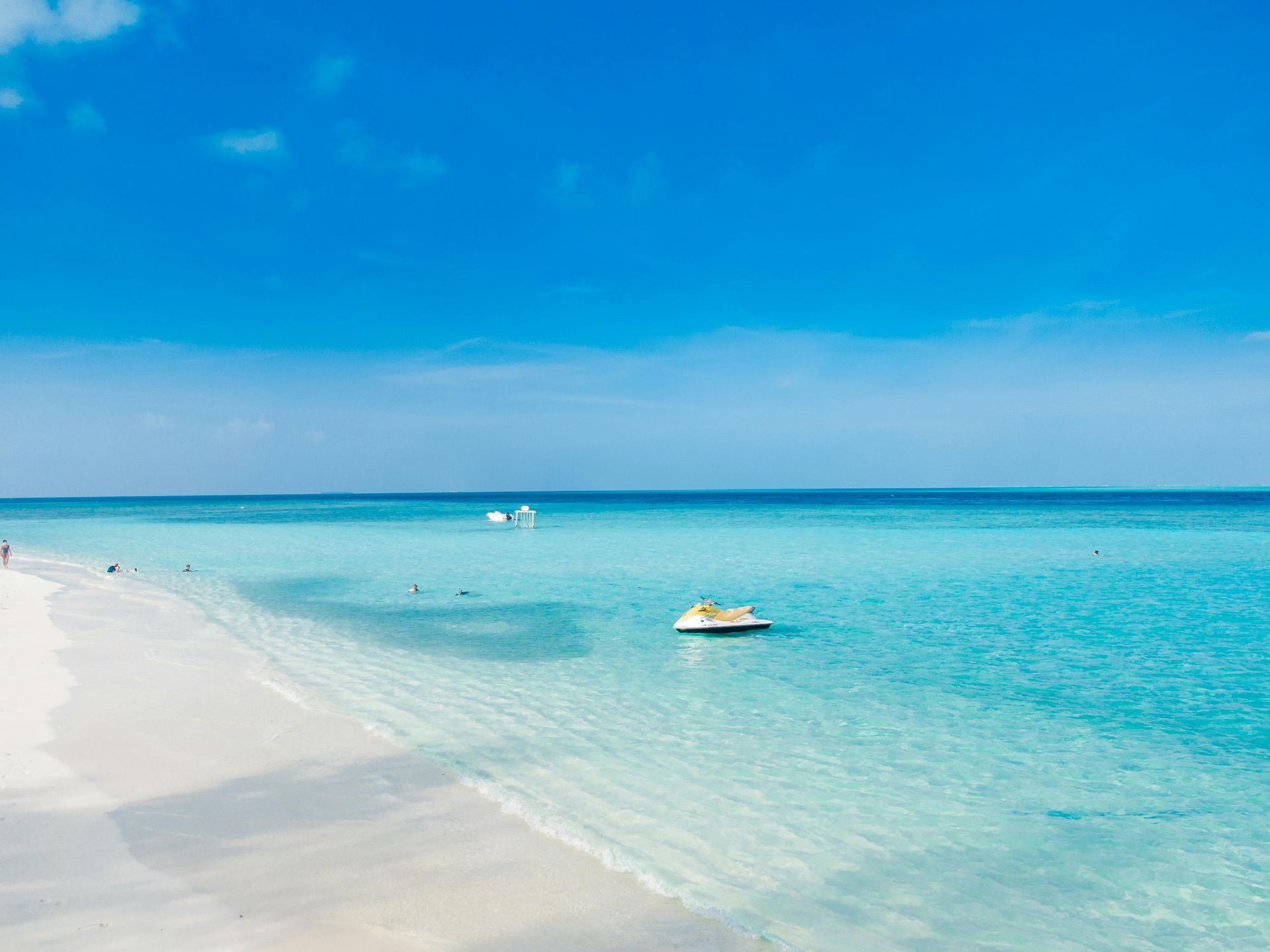 Tropical beach with white sand, turquoise water, and a small boat under a bright blue sky