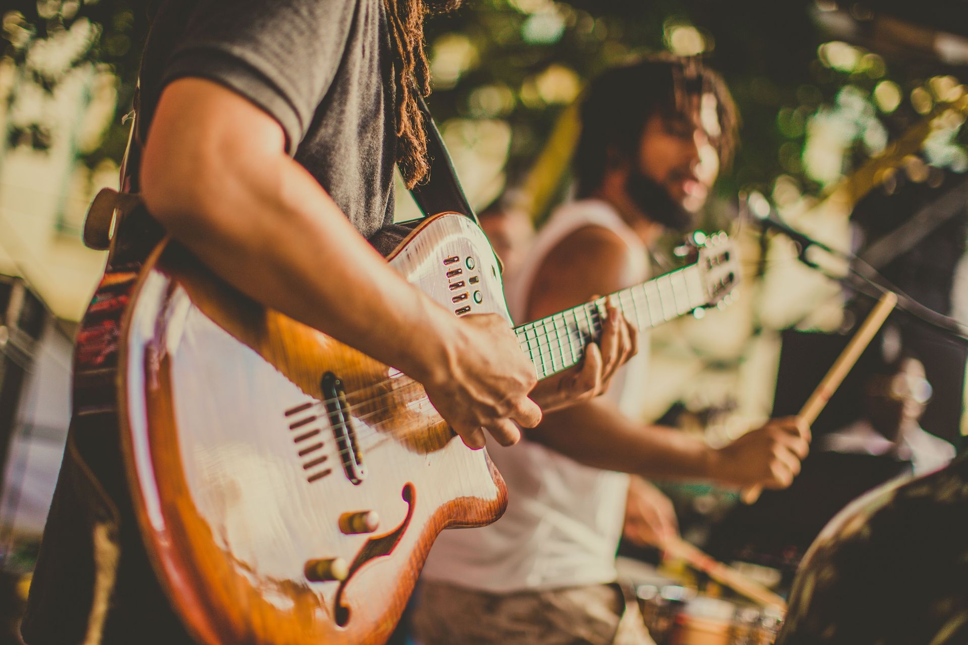 Musicians playing guitar and drums on an outdoor stage at sunset