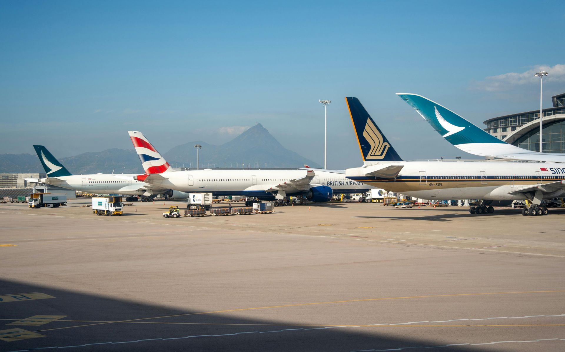Airplanes parked on an airport tarmac with mountains in the background and a blue sky