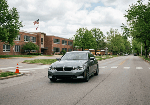Gray BMW sedan driving through a school zone near a crosswalk and school buses