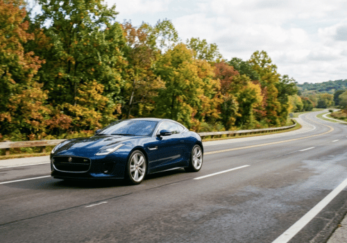 Blue Jaguar sports car driving along a scenic highway surrounded by fall foliage