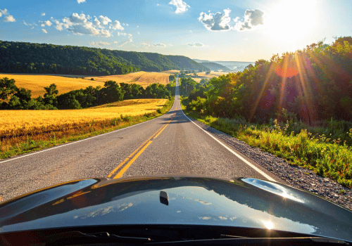 View from a car driving down a scenic country road with rolling hills and bright summer sunlight.
