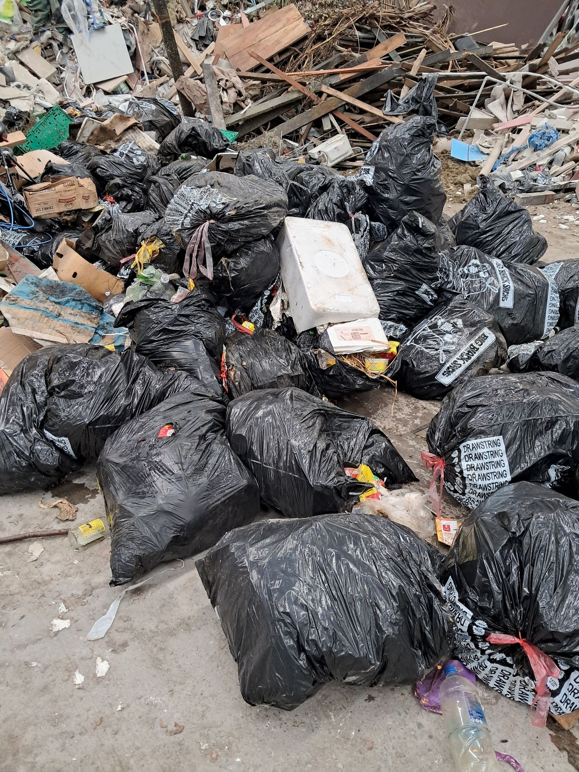 A pile of black garbage bags and scattered debris on a concrete surface. A pile of black garbage bags and scattered debris on a concrete surface.