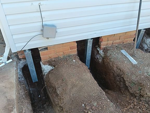 House lifted on jacks over dug-out foundation trenches and soil piles