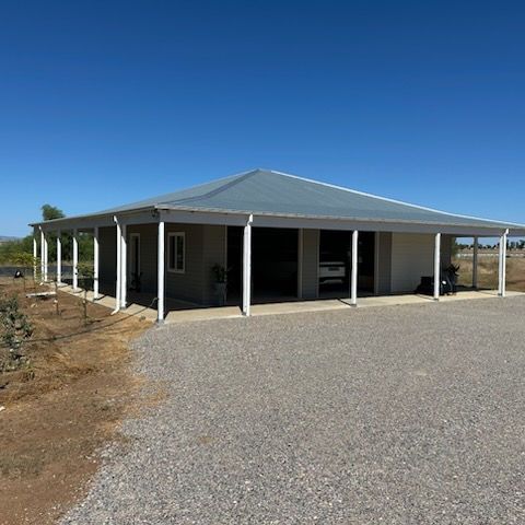 Single-story house with gray metal roof, white porch columns, and gravel driveway under a clear blue sky