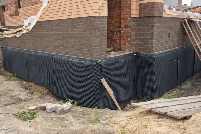 Black waterproofing membrane around a brick house foundation under construction