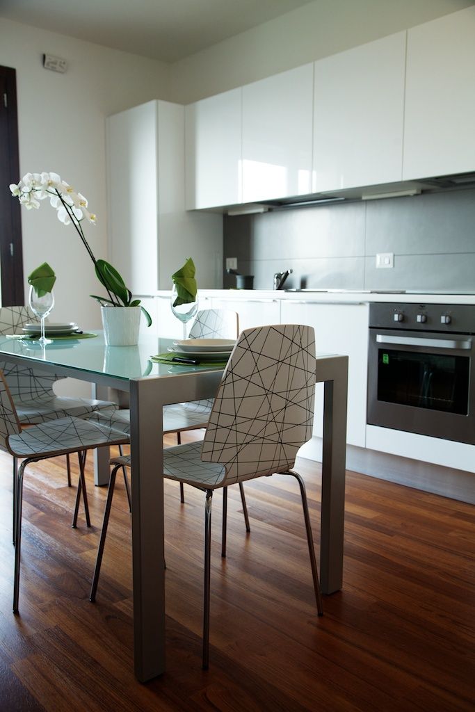 Cucina moderna con pavimenti in legno, mobili bianchi, tavolo da pranzo con sedie e forno.