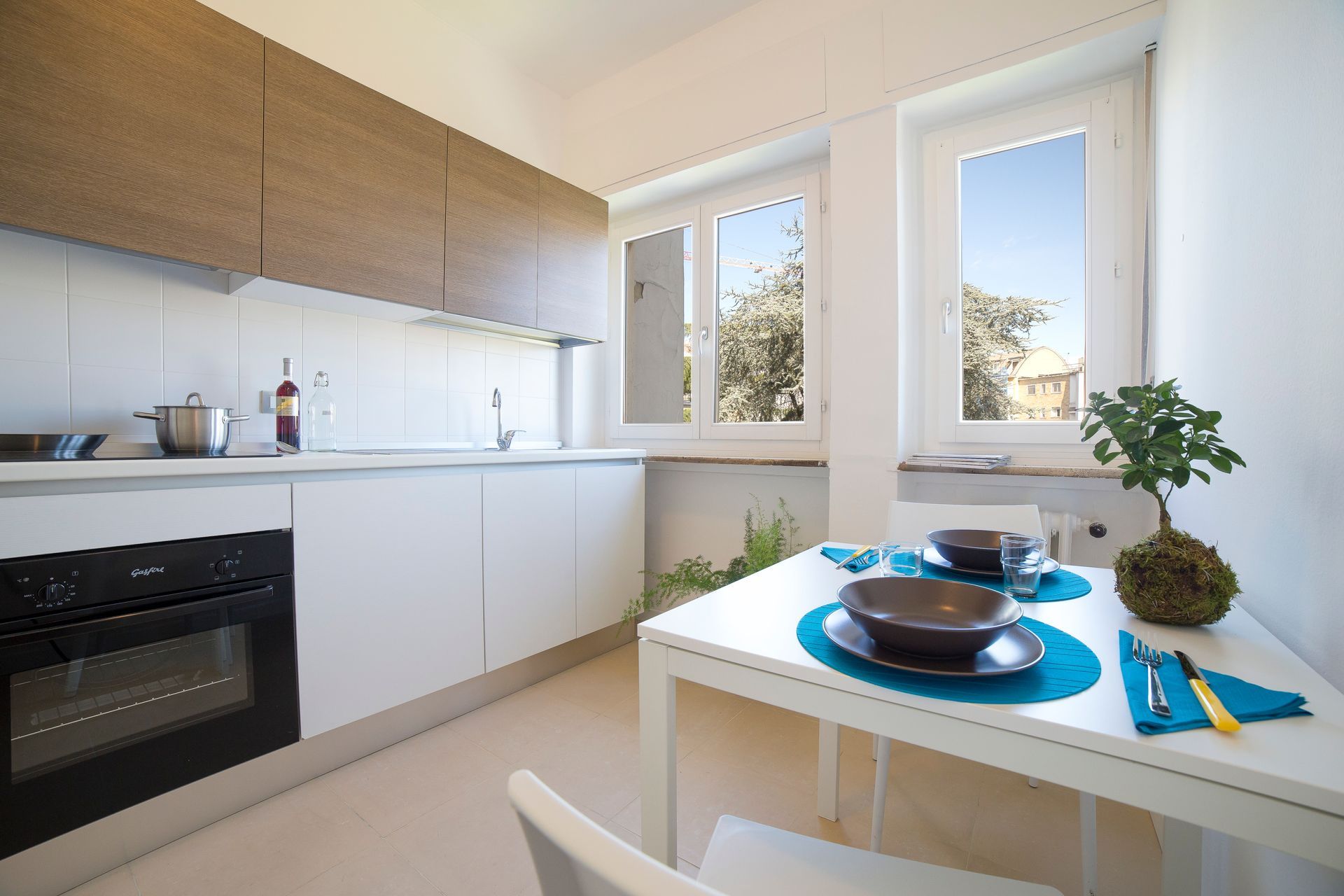 Cucina moderna con mobili bianchi, dettagli in legno e piccolo tavolo da pranzo.