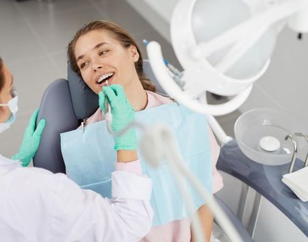 Dentist examining a smiling patient in a bright dental clinic, with gloved hands and a bib.