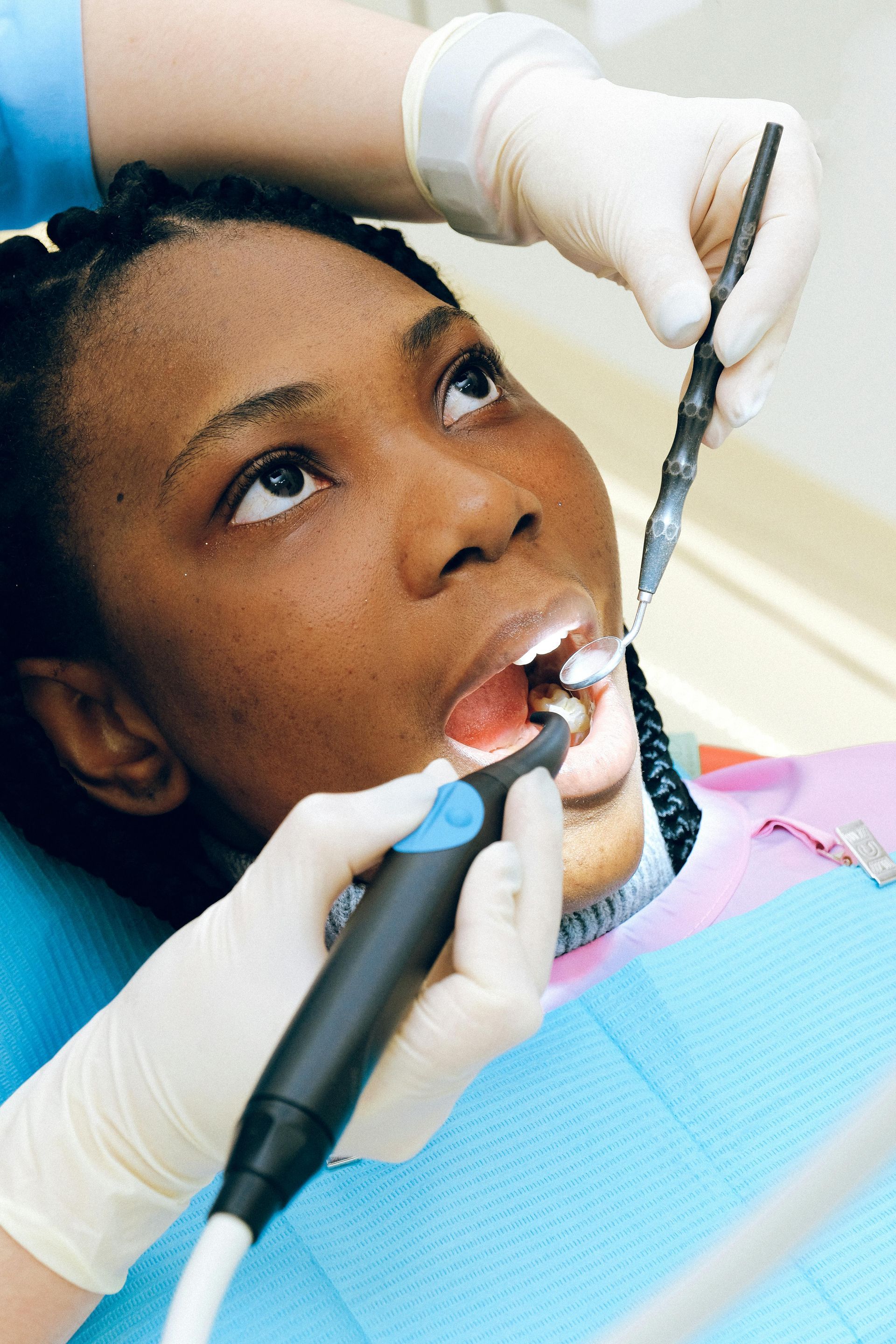 A dentist performing a dental examination on a patient using a mirror and a handpiece.