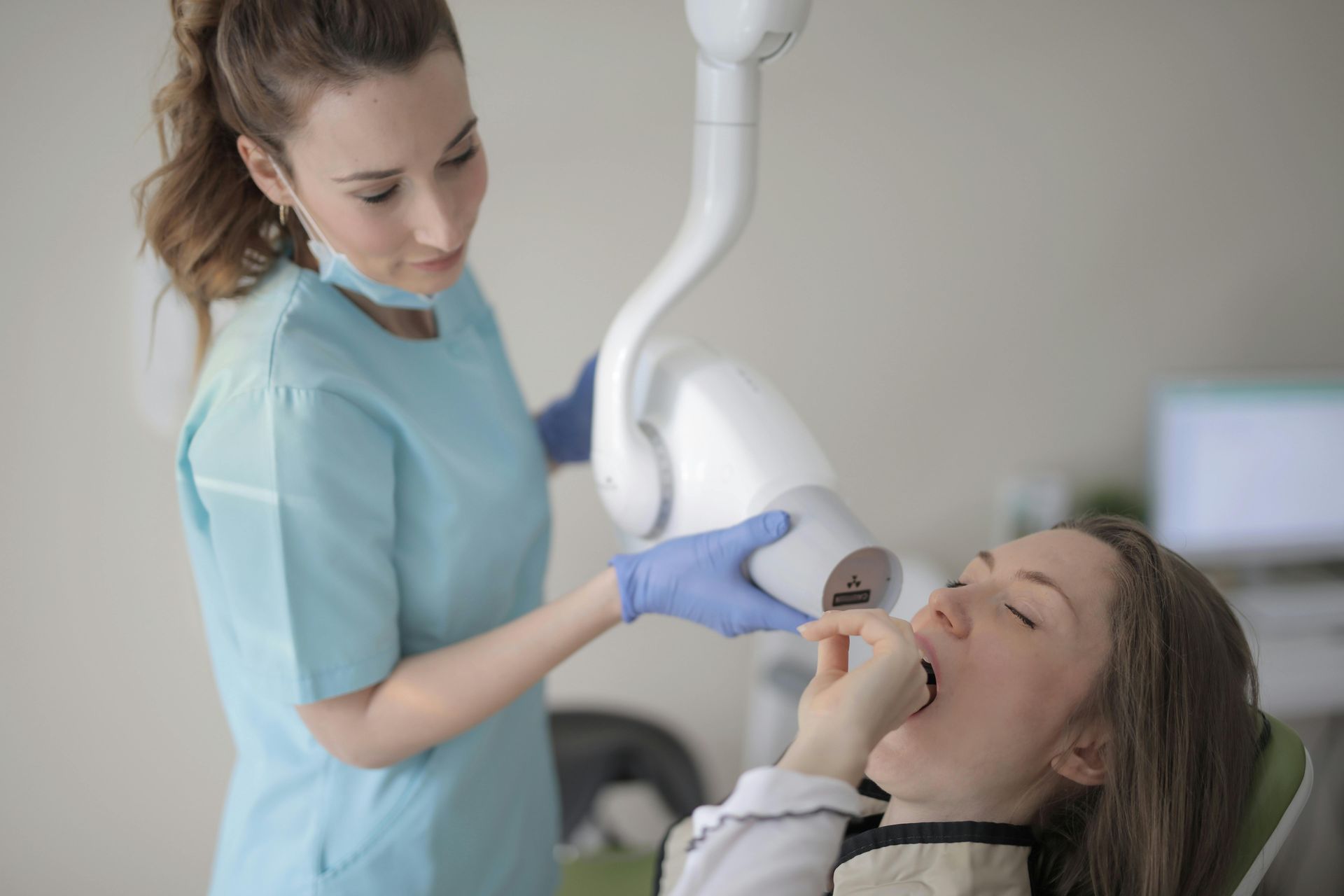 A dental professional using a handheld X-ray device on a patient sitting in a dental chair.