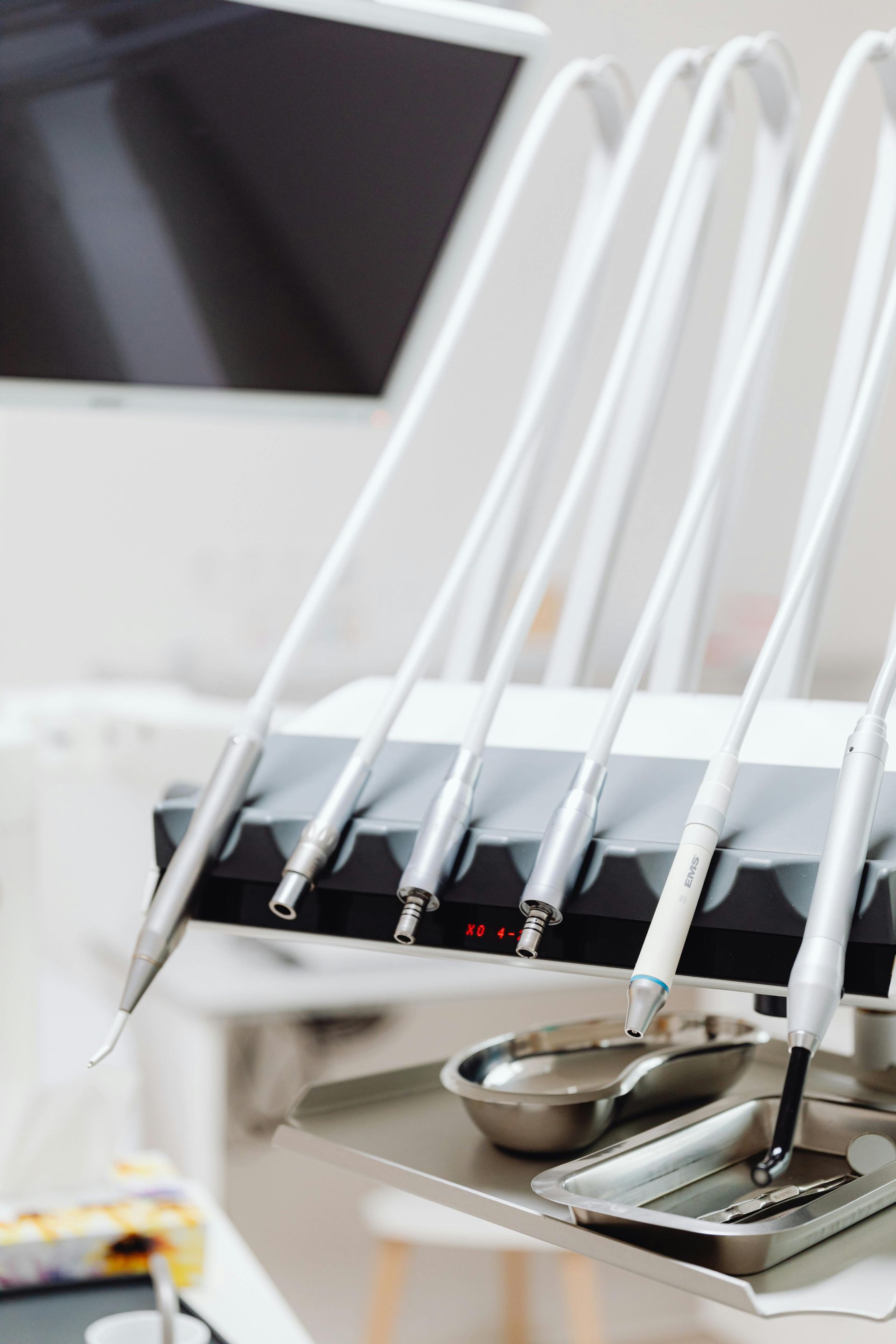 Dental equipment rack with various handpieces, hoses, and a metal tray in a bright, clinical medical setting.