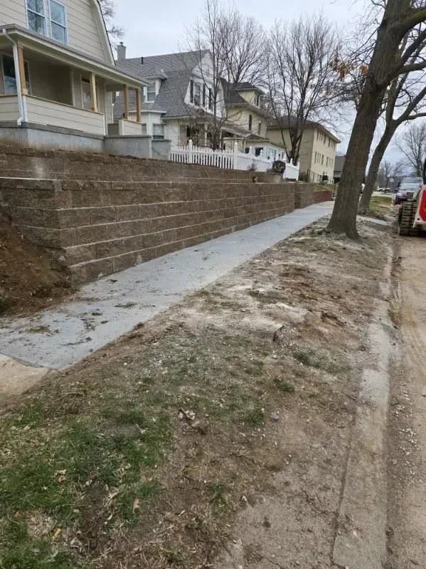 A brick wall along a sidewalk next to a house.