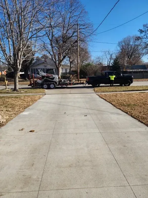 A truck is towing a lawn mower down a driveway.