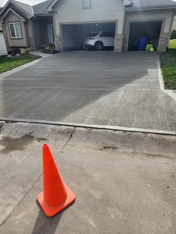 An orange traffic cone is sitting on the side of a driveway in front of a house.