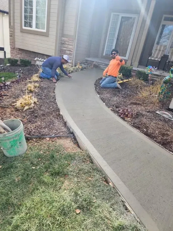 Two men are working on a concrete walkway in front of a house.