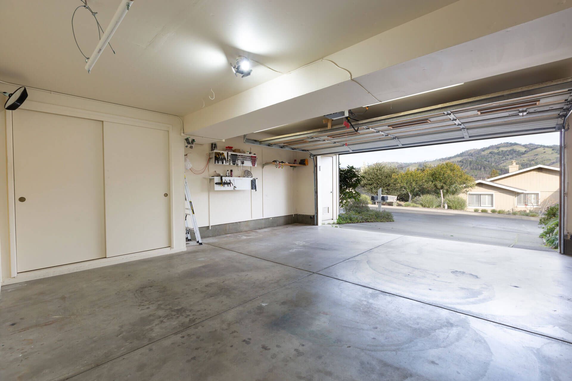 An empty garage with the door open and a house in the background.